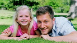 Video: Man looks at his daughter with a confused look before smiling as they lie on the grass Man looks at his daughter with a confused look before smiling as they lie on the grass