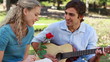 Boyfriend plays guitar for his girlfriend as she holds a rose and then kiss
