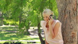 Video: A woman standing by a tree talking on her phone as she hangs up at looks at the camera A woman standing by a tree talking on her phone as she hangs up at looks at the camera