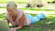 A camera pans past a woman lying down and using her laptop