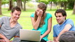 Video: Three friends talking while looking at a laptop as they sit in a park Three friends talking while looking at a laptop as they sit in a park