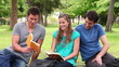 Video: Man shows a book to his friends while smiling as they sit together in a park Man shows a book to his friends while smiling as they sit together in a park
