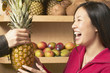 Asian woman holding pineapple in grocery store