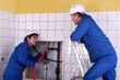 Apprentice passing red cable up behind a tiled wall