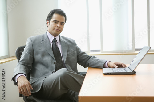 Photo: Portrait of businessman sitting at desk with laptop computer Portrait of businessman sitting at desk with laptop computer