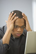 Man sitting at desk in front of computer with hands on head