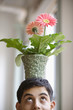 Close up of young adult man balancing potted flower on head