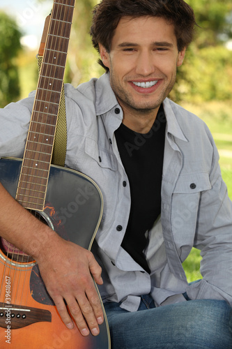 Photo: Young man sitting in a park with his guitar Young man sitting in a park with his guitar