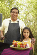 Hispanic father and daughter next to barbecue grill with kebabs