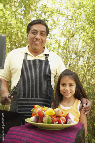 Photo: Hispanic father and daughter next to barbecue grill with kebabs Hispanic father and daughter next to barbecue grill with kebabs
