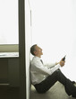 Asian businessman sitting against cubicle wall with telephone