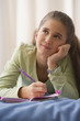 Hispanic girl writing in diary on bed