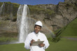 Man with hard hat and clipboard in front of waterfall