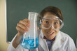 Boy wearing lab coat and goggles and holding steaming beaker in classroom