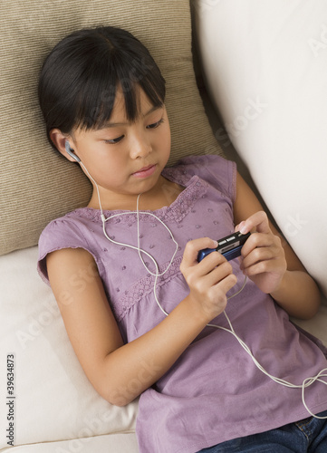 Photo: Young Asian girl listening to mp3 player on sofa Young Asian girl listening to mp3 player on sofa
