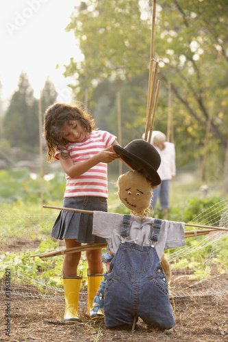 Photo: Young Hispanic girl putting hat on scarecrow Young Hispanic girl putting hat on scarecrow