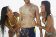 Two women rubbing sand on man at beach