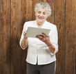 portrait of senior woman touching digital tablet against a woode