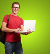 portrait of young man holding laptop and wearing backpack over g