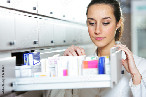 Photo: Young female pharmacist reaching for medicine Young female pharmacist reaching for medicine