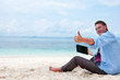 Photo: Business man sitting and working on the beach with tablet comput Business man sitting and working on the beach with tablet comput