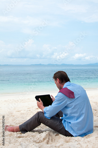 Photo: Business man working on the beach with tablet computer Business man working on the beach with tablet computer