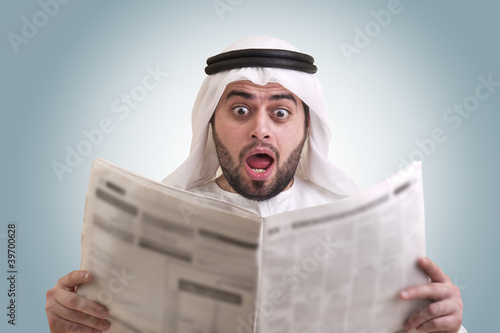 Photo: arabian businessman shocked while reading newspaper arabian businessman shocked while reading newspaper