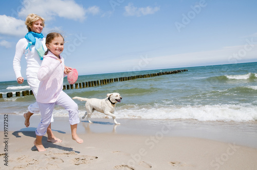 Photo: Happy family playing with dog on the beach Happy family playing with dog on the beach