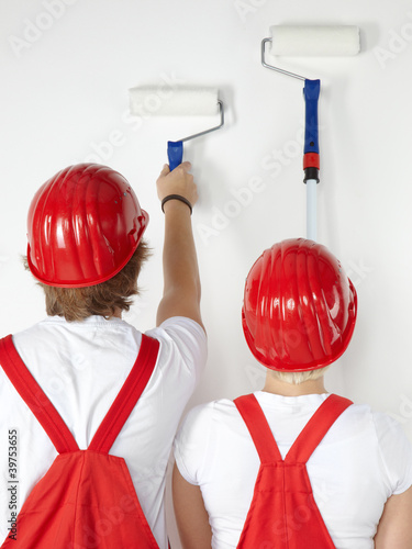 Foto: Young worker couple is painting a white wall Young worker couple is painting a white wall