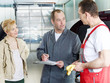 Master mechanic and his worker in a garage with female customer