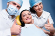 Dentist with assistant and smiling patient showing  thumb up