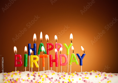Photo: Happy birthday lit candles on brown background Happy birthday lit candles on brown background