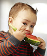 portrait of a handsome kid bitting a watermelon piece indoor