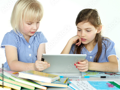 Photo: Two cute girlfriends learning with books and touchpad Two cute girlfriends learning with books and touchpad