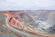 Big mine pit with little dump trucks and reddish soil