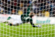Goalkeeper is catching a football, visible trough the goal net