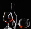 Glasses of brandy and bottle on black background
