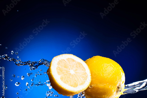 Foto: Fresh lemon and half of lemon in the splashes of water on a dark Fresh lemon and half of lemon in the splashes of water on a dark