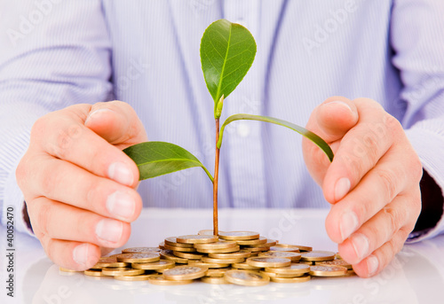 Photo: Business man hands with a tree growing from pile of coins Business man hands with a tree growing from pile of coins