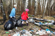 Back of brother and sister with black bags collect trash in park