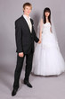 Beautiful bride and groom hold hands and stand in studio on gray