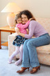 Smiling mother and daughter sit on couch and hug in cozy room