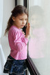 Little beautiful sad girl looks out window and touches glass