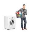 Man with laundry basket posing next to a washing machine