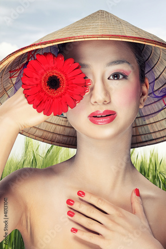 Photo: Beautiful vietnamese girl in a traditional hat is holding flower Beautiful vietnamese girl in a traditional hat is holding flower