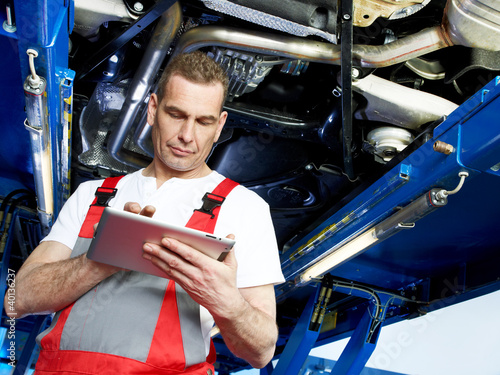 Photo: Motor mechanic works under the service lift with his touchpad Motor mechanic works under the service lift with his touchpad