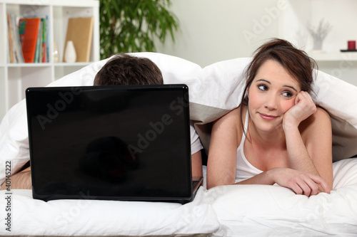 Photo: Bored woman next to boyfriend in bed Bored woman next to boyfriend in bed