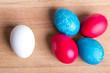 Four colored Easter eggs and white, on a piece of wood Four colored Easter eggs and white, on a piece of wood