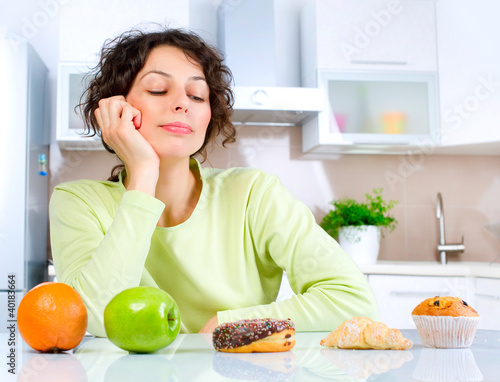 Photo: Diet. Beautiful Young Woman choosing between Fruits and Sweets Diet. Beautiful Young Woman choosing between Fruits and Sweets