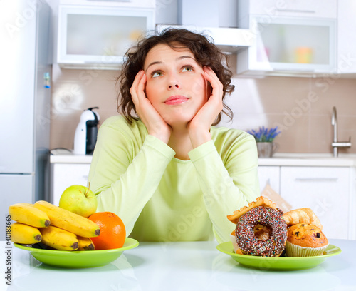 Photo: Beautiful Young Woman choosing between Fruits and Sweets Beautiful Young Woman choosing between Fruits and Sweets